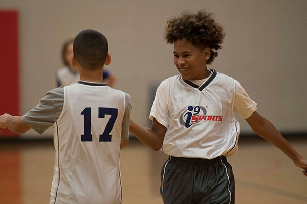 Smiling basketball player in white i9 Sports jersey gives a high five to a teammate