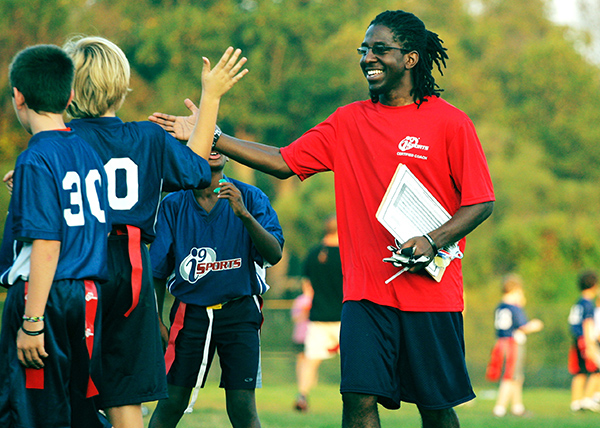 i9 Sports coach gives a kid flag football player a high five at the end of the game.