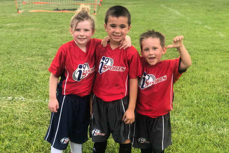Three kids soccer players in red jerseys smile together